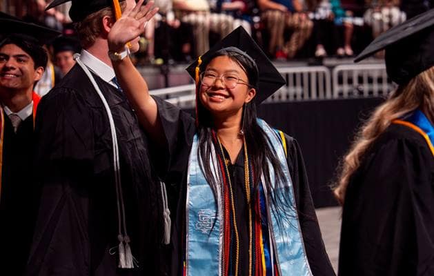 Graduate waves at crowd at Prescott spring commencement.