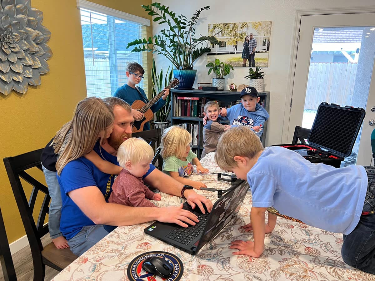 Father works on a laptop with kids around.