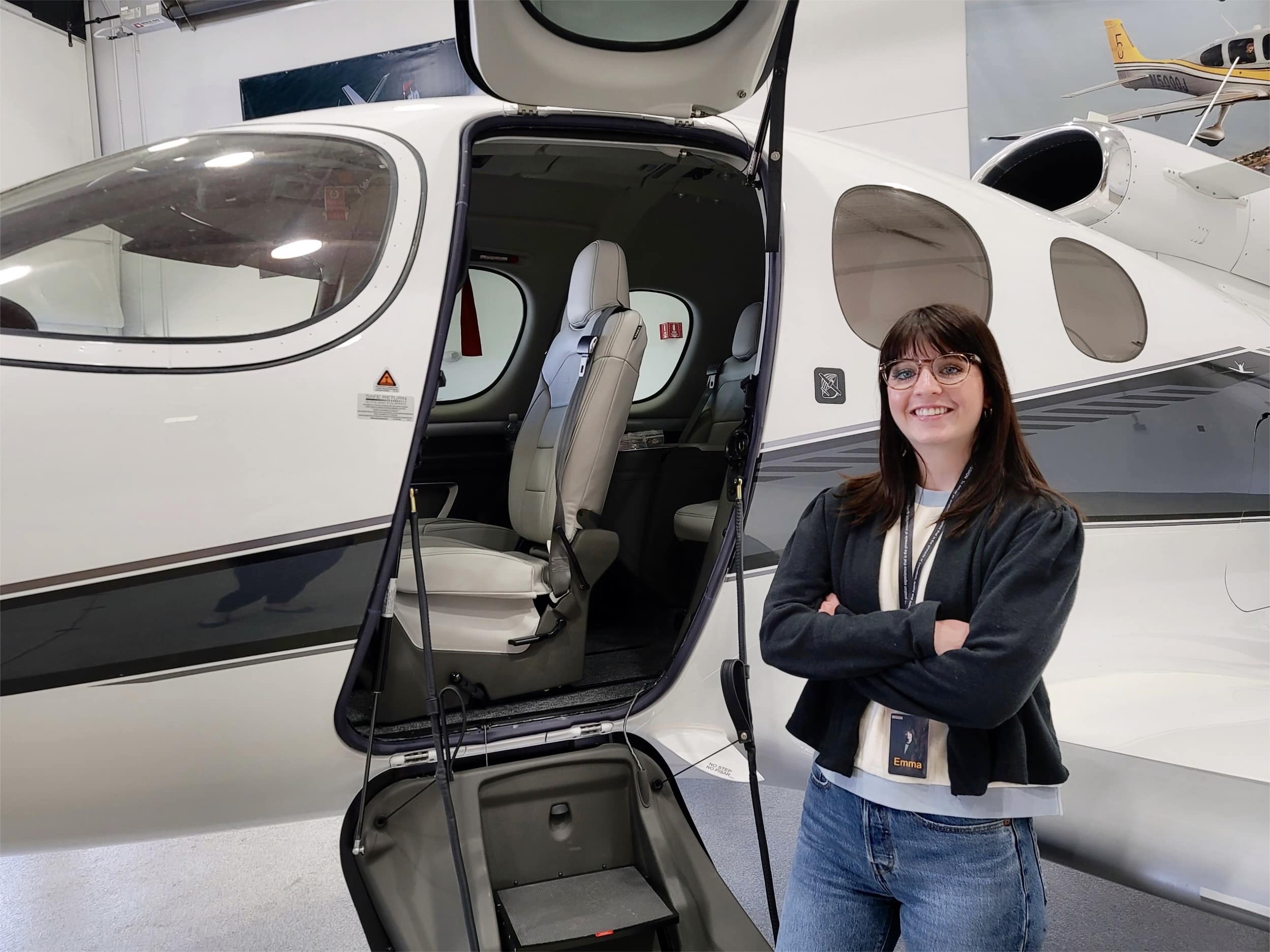 Emma Rasmussen standing in front of a Cirrus Aircraft in Black Jacket
