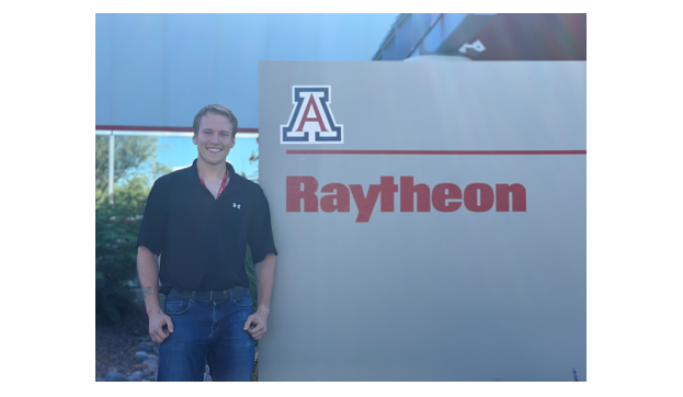 photo of Johnathan Henry standing by Raytheon sign