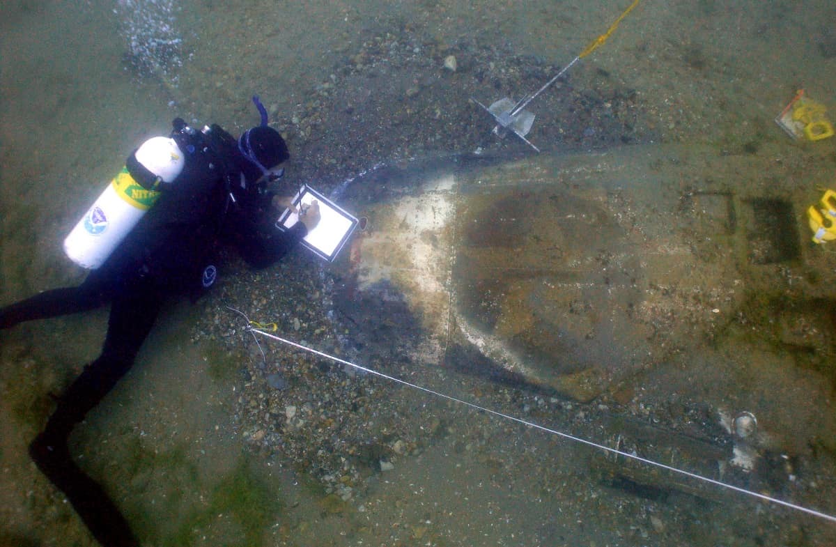 Erik Denson scuba dives near underwater wreckage.