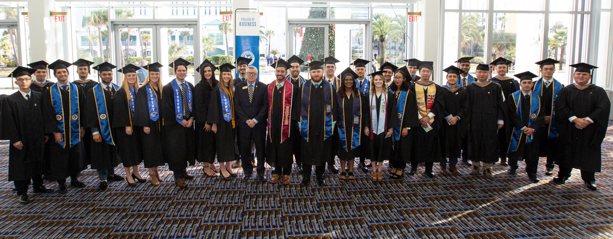 College of Business grads wearing graduation robes and caps, in the ICI Center atrium.