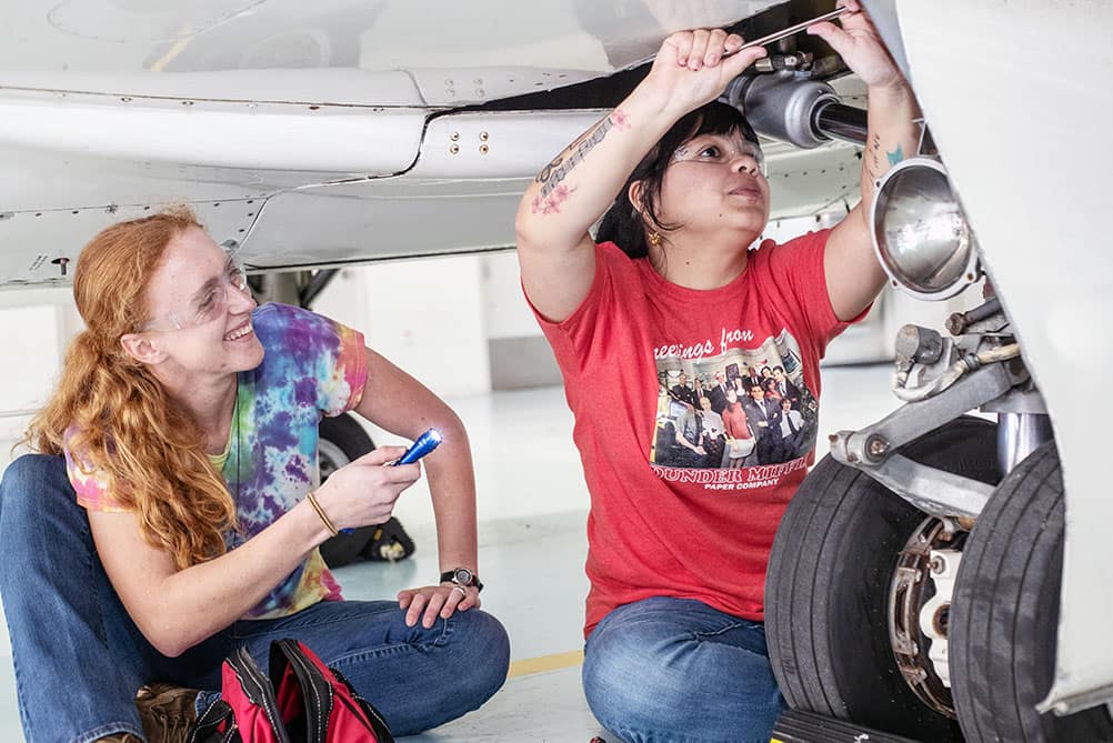 Two female AMS students inspecting landing gear on small aircraft