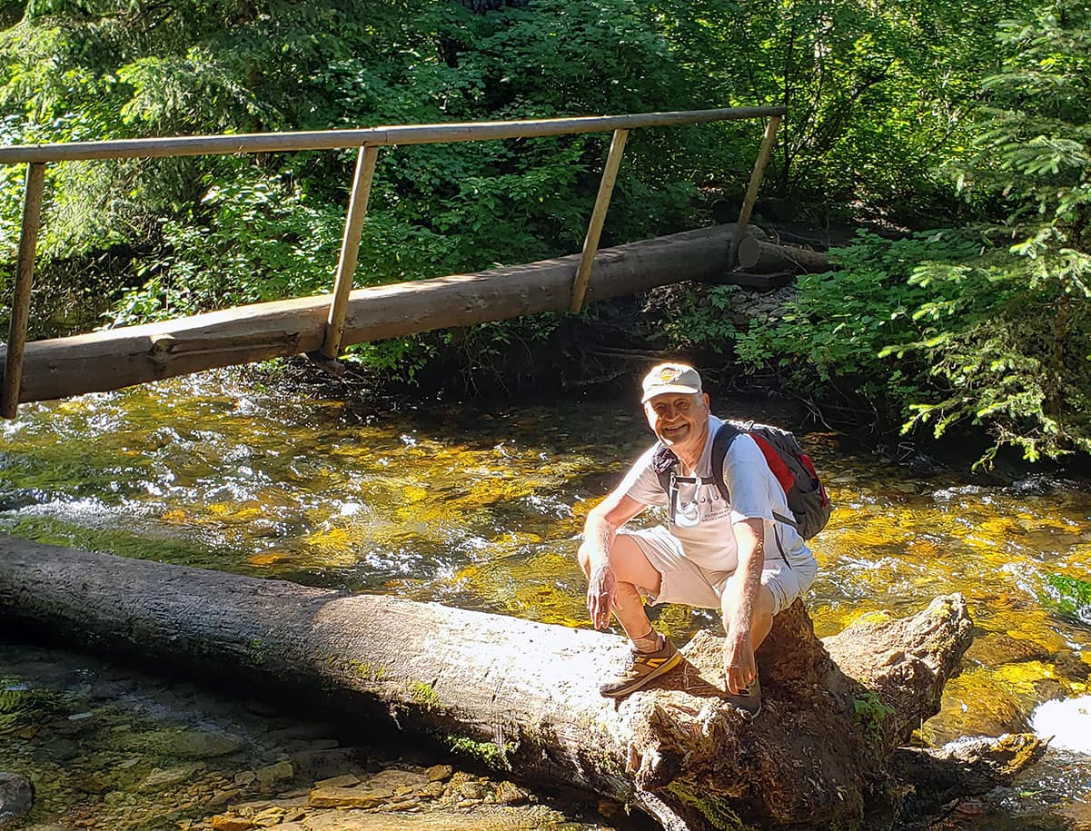 Warren Childers sitting on a log by a stream