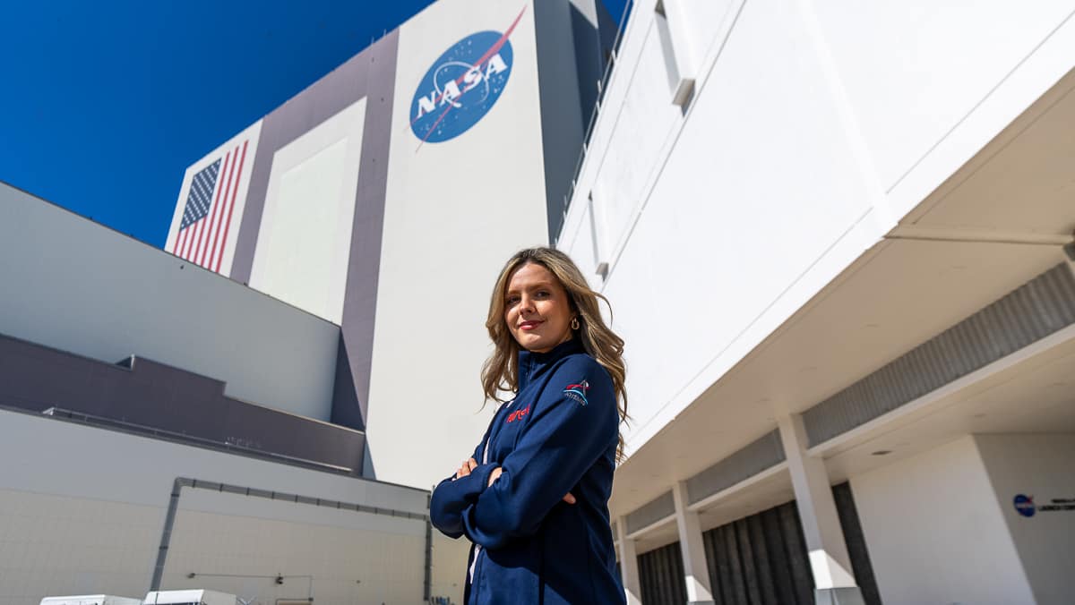 Woman stands in NASA uniform in front of NASA sign and building