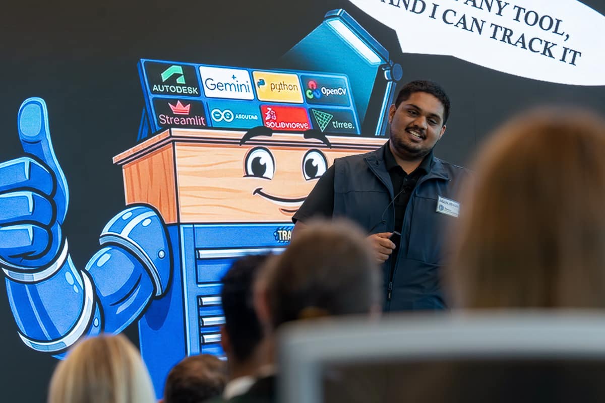 Man speaks to audience with large drawing of tool chest making a thumbs up behind