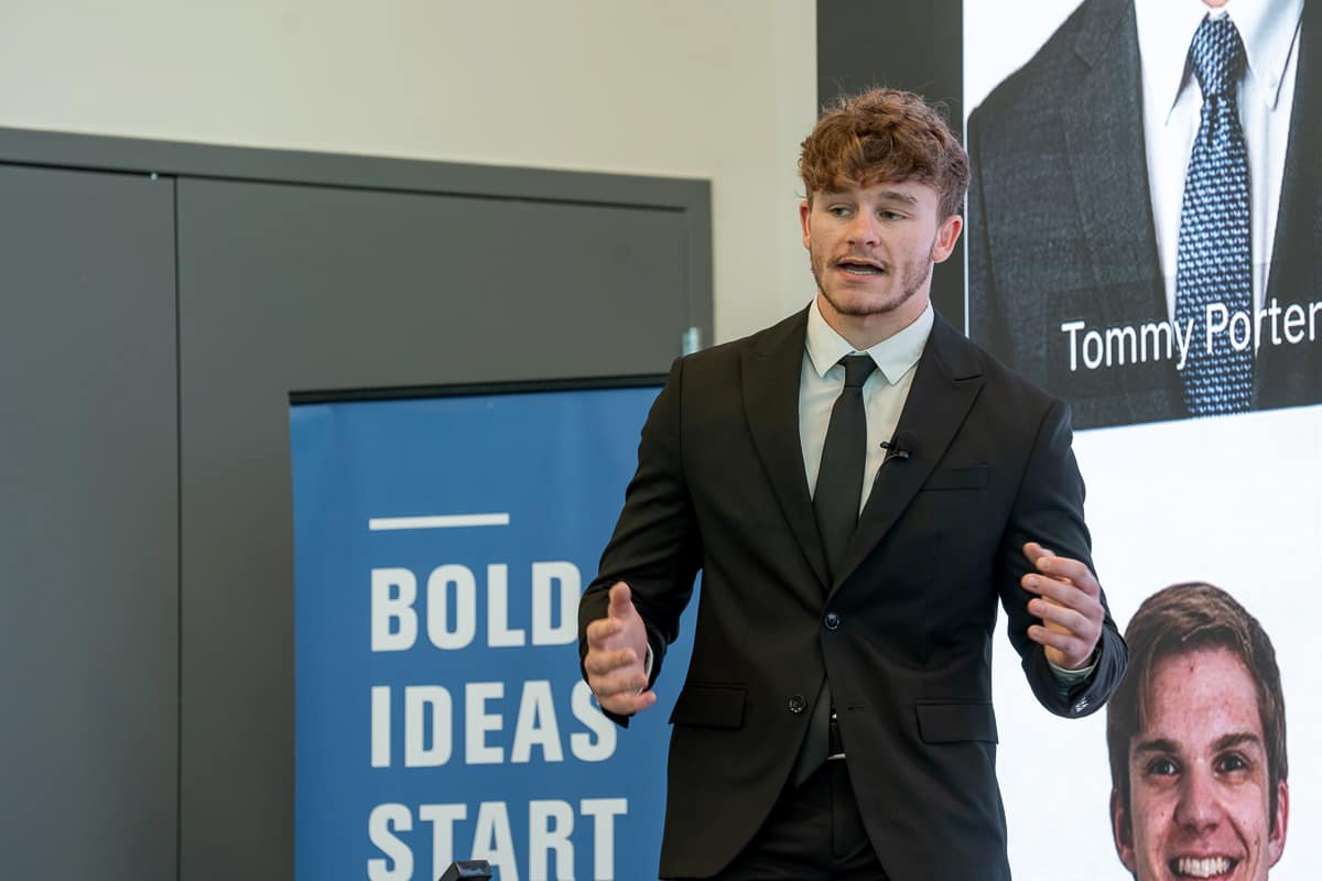 Young man in suit speaks in front of screen