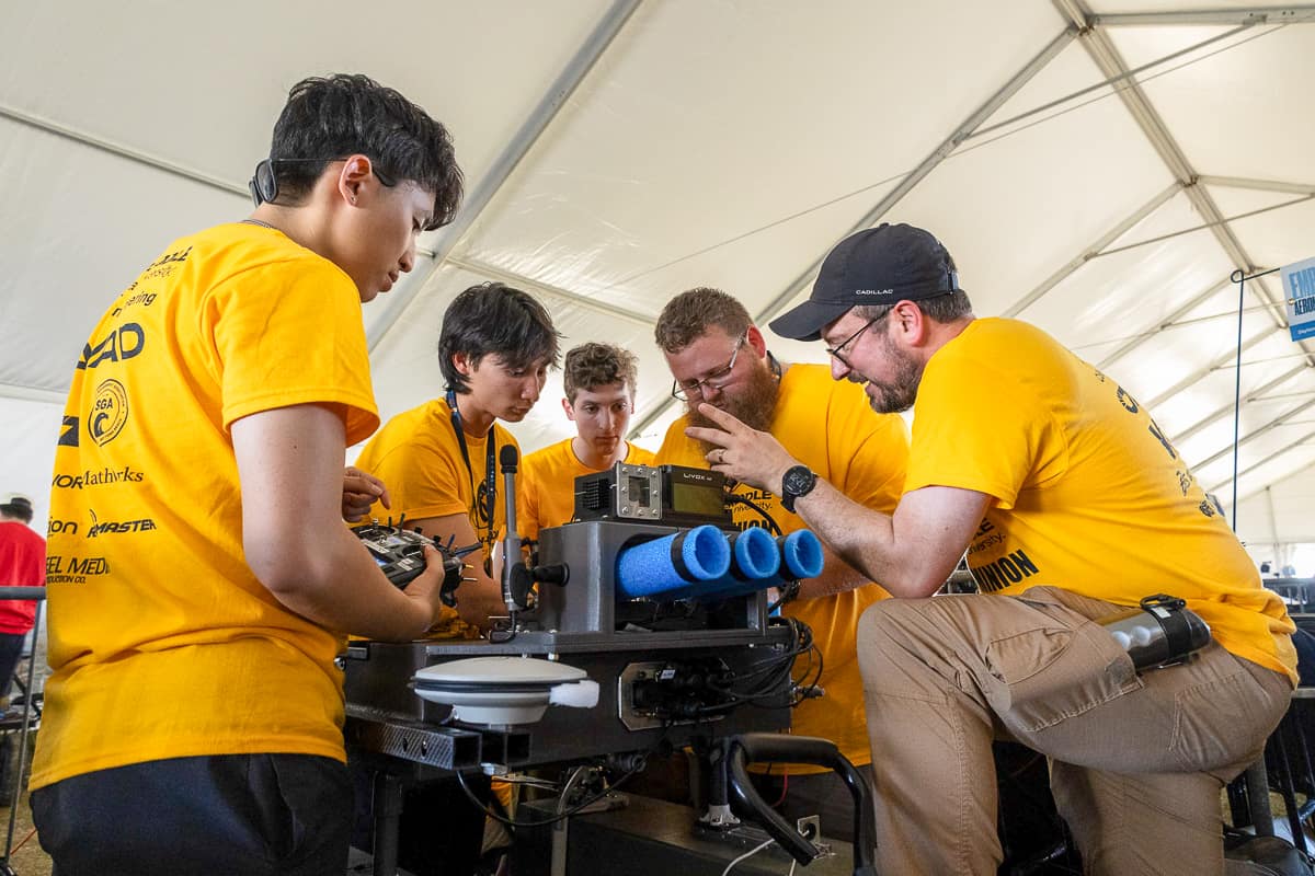 Five men in yellow shirts work on a robotic boat