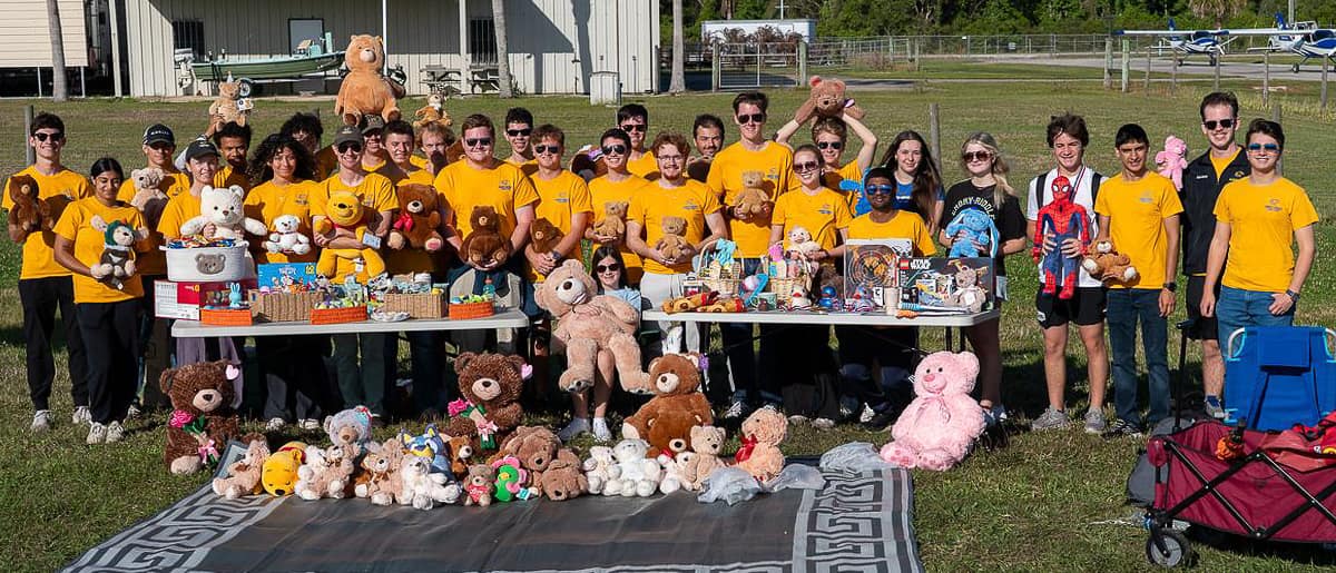Twenty-eight young men and women stand in a row, some holding teddy bears