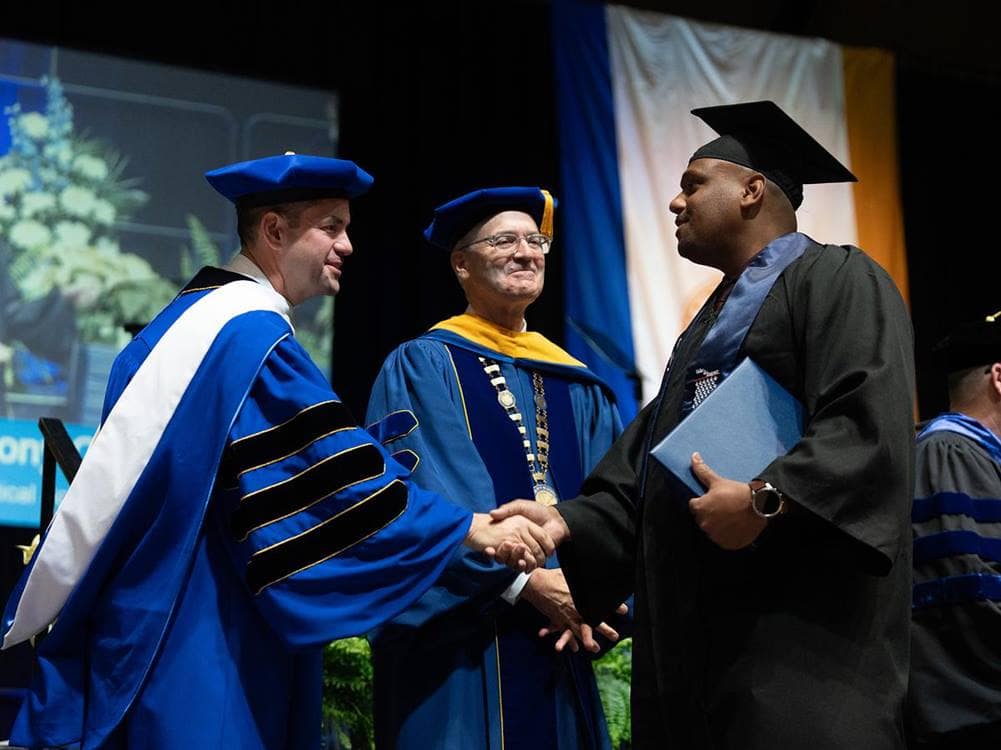 Astronaut and alumnus Jared Isaacman shakes hands with an Embry-Riddle student receiving his diploma