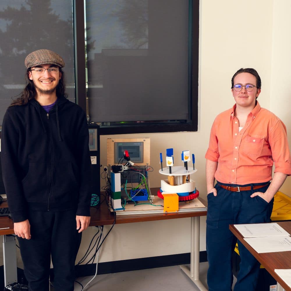 Students Austin Palahnuk and Wrin Monger stand beside their carnival game that uses artificial intelligence to automatically track and shoot rotating banana targets. 