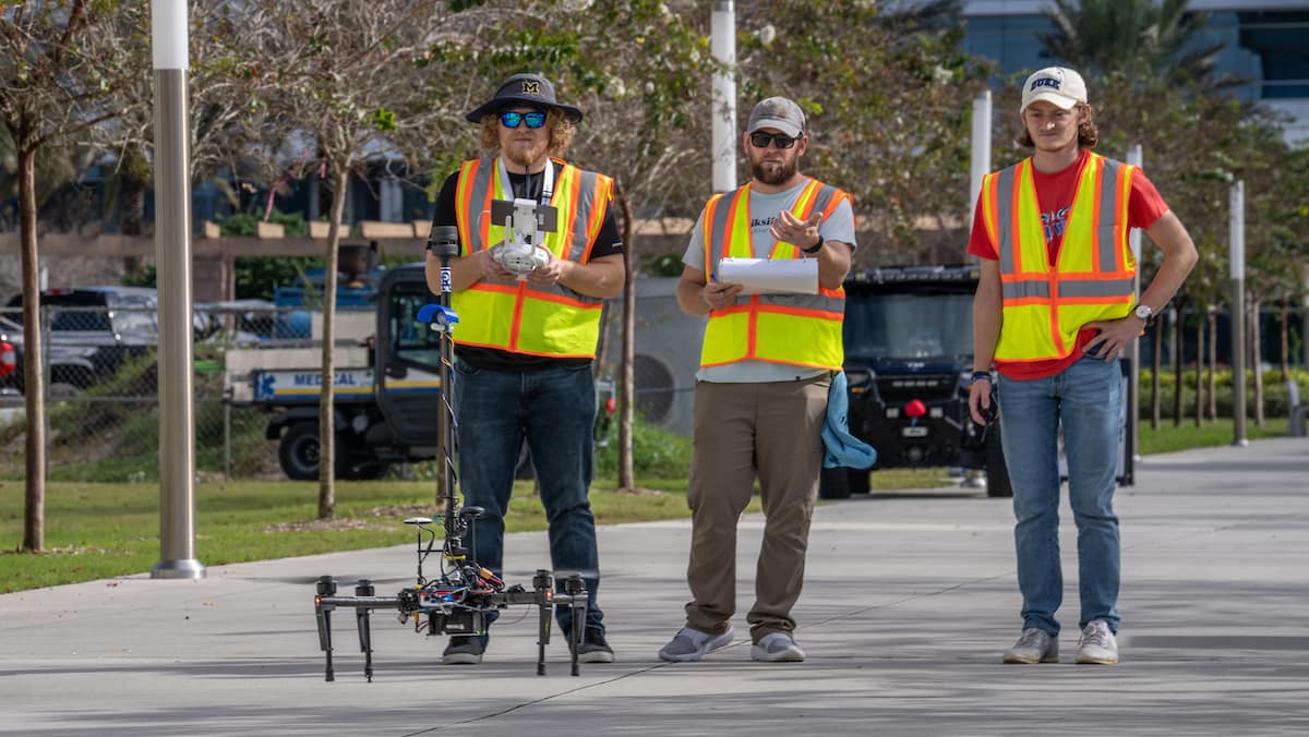 Three students look at a landed drone