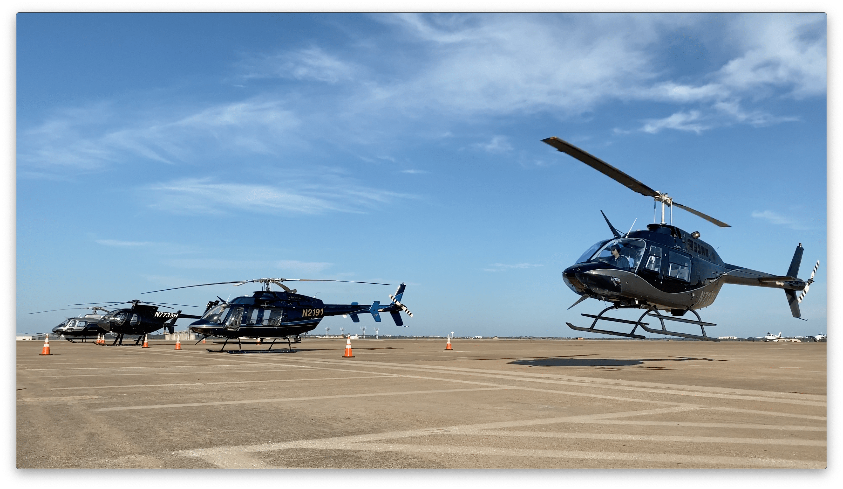 Helicopter landing on a paved lot with two other helicopters on the ground