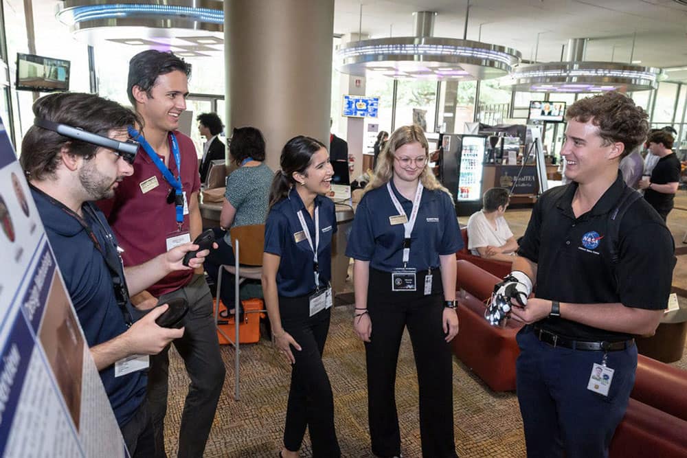 Joseph DeMartini, Cole Montrose, Joyce Garcia and Miranda Young look on as Jon Guthmiller, a recent Embry-Riddle graduate who now works in mission control at Johnson Space Center, tries on their glove prototype