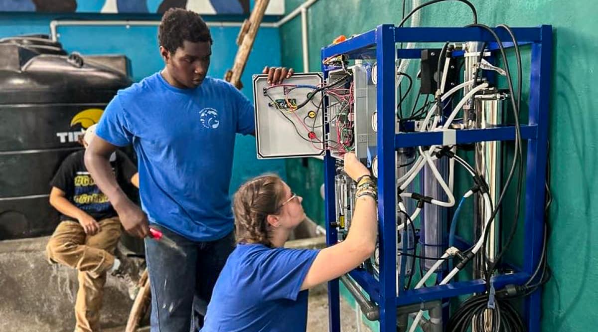 Students Zoey Hart and David Njuguna work on the electrical components of the solar-powered water purification system, which the Pure Water Project installed at a community center in the Dominican Republic.