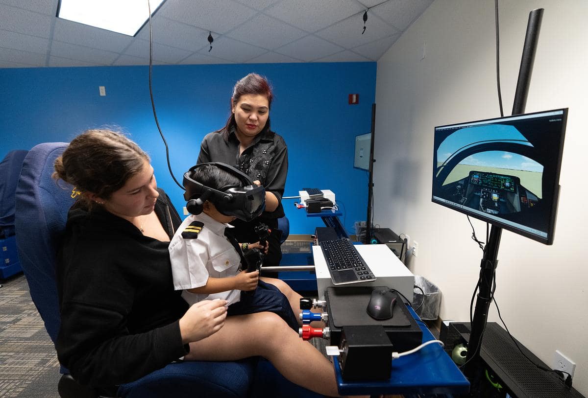 With his mother, Rowena Santos, looking on, Kryzian wears virtual reality goggles while he sits with Flight student Allison Booher.
