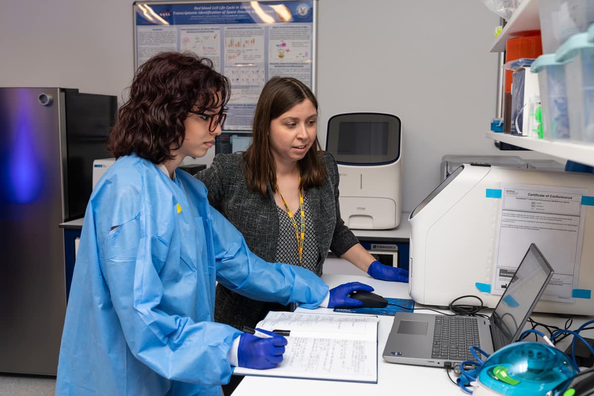 Dr. Sen Kilic discusses gene expression results with Aerospace Physiology student Valeria Jimenez, referring to her experimental notes.