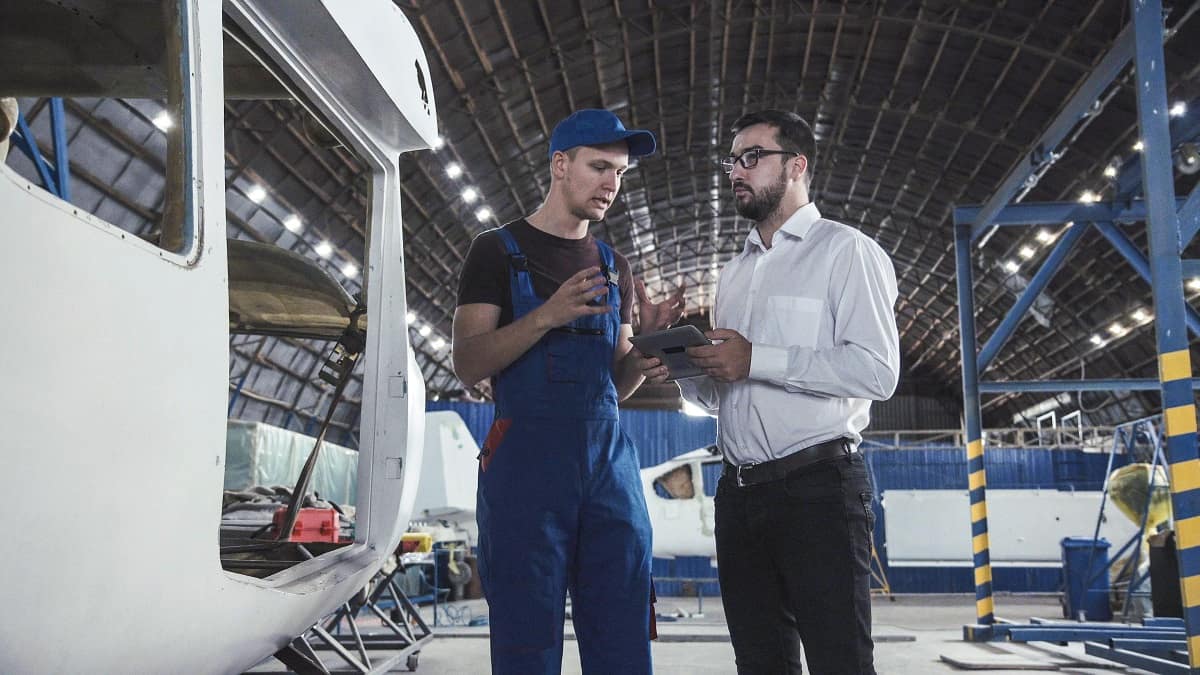 Mechanic and Engineer talk in a hangar near airplanes.