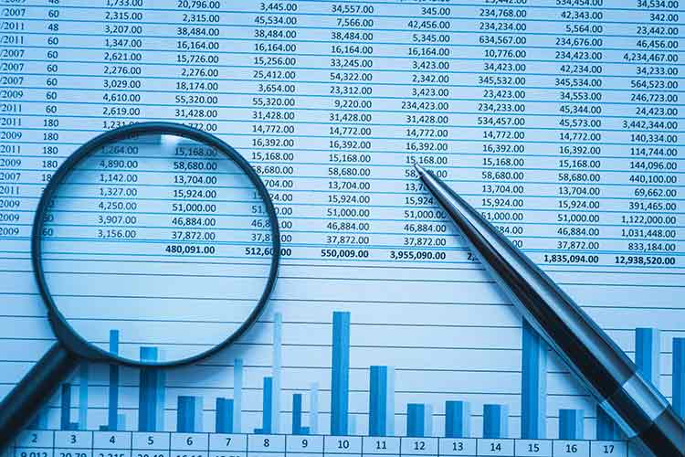 A magnifying glass and pen rest on a paper with bar graphs and numbers.