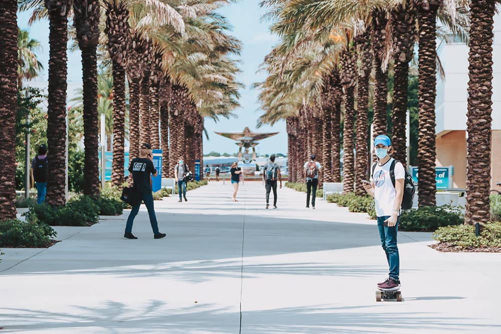 Student wearing mask rides skateboard on Embry-Riddle campus in Daytona Beach
