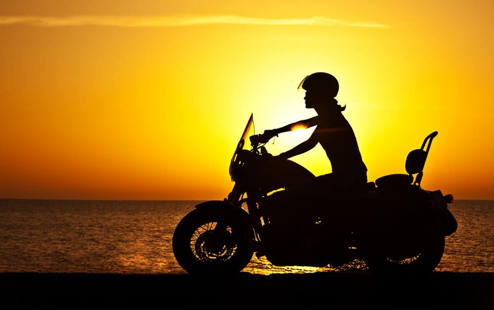 Biker rides along the coast with sun in background
