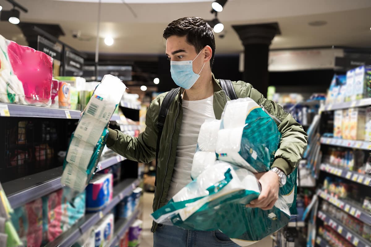 A young man in a mask buys toilet paper at a supermarket.
