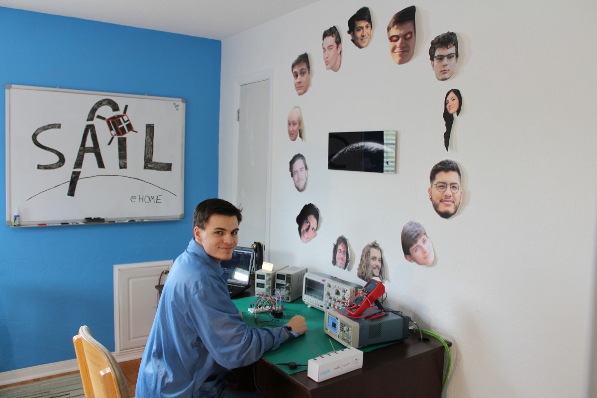 Space and Atmospheric Instrumentation Lab (SAIL) student Nathan Graves designed his SAIL@home set-up to feature the SAIL logo along with photos of classmates hanging prominently above his desk’s array of lab equipment.