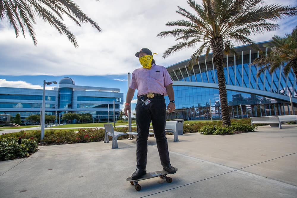 Student wearing bandana rides skateboard through campus